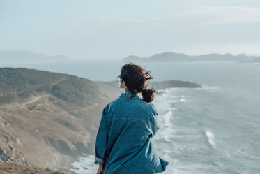 person takes in the view of wavy waters and hills below