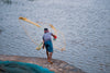 person throws fishing net into blue water from the shore