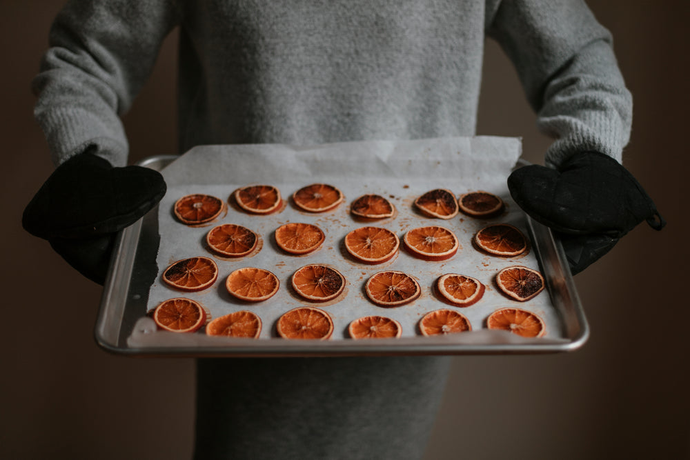 person tilts silver tray filled with baked oranges forward