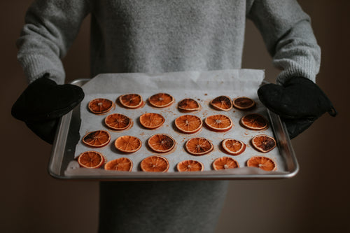 person tilts silver tray filled with baked oranges forward