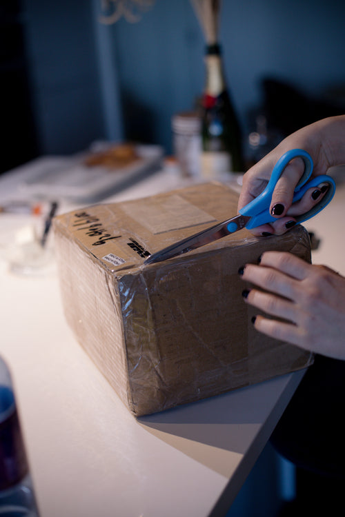 person uses scissors to cut open a taped cardboard box