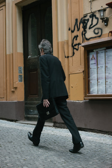 person walks quickly with bags by a brown building