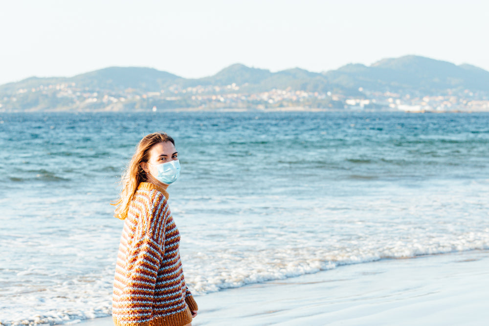 person walks the beach while wearing a facemask