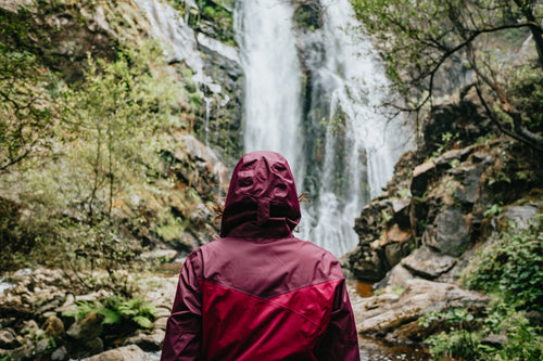 person wearing a raincoat looks at tall waterfall
