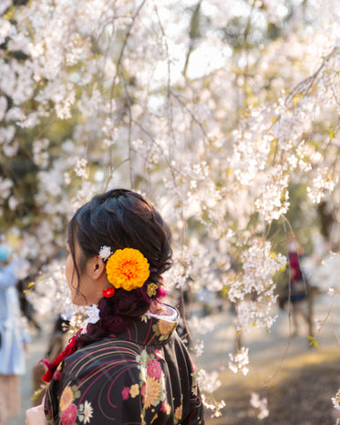 person with an orange flower stands under blossoming tree