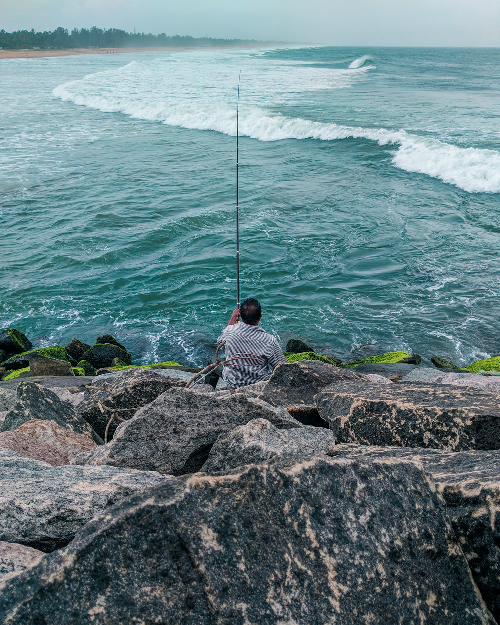 person with fishing rod of mossy green rocks