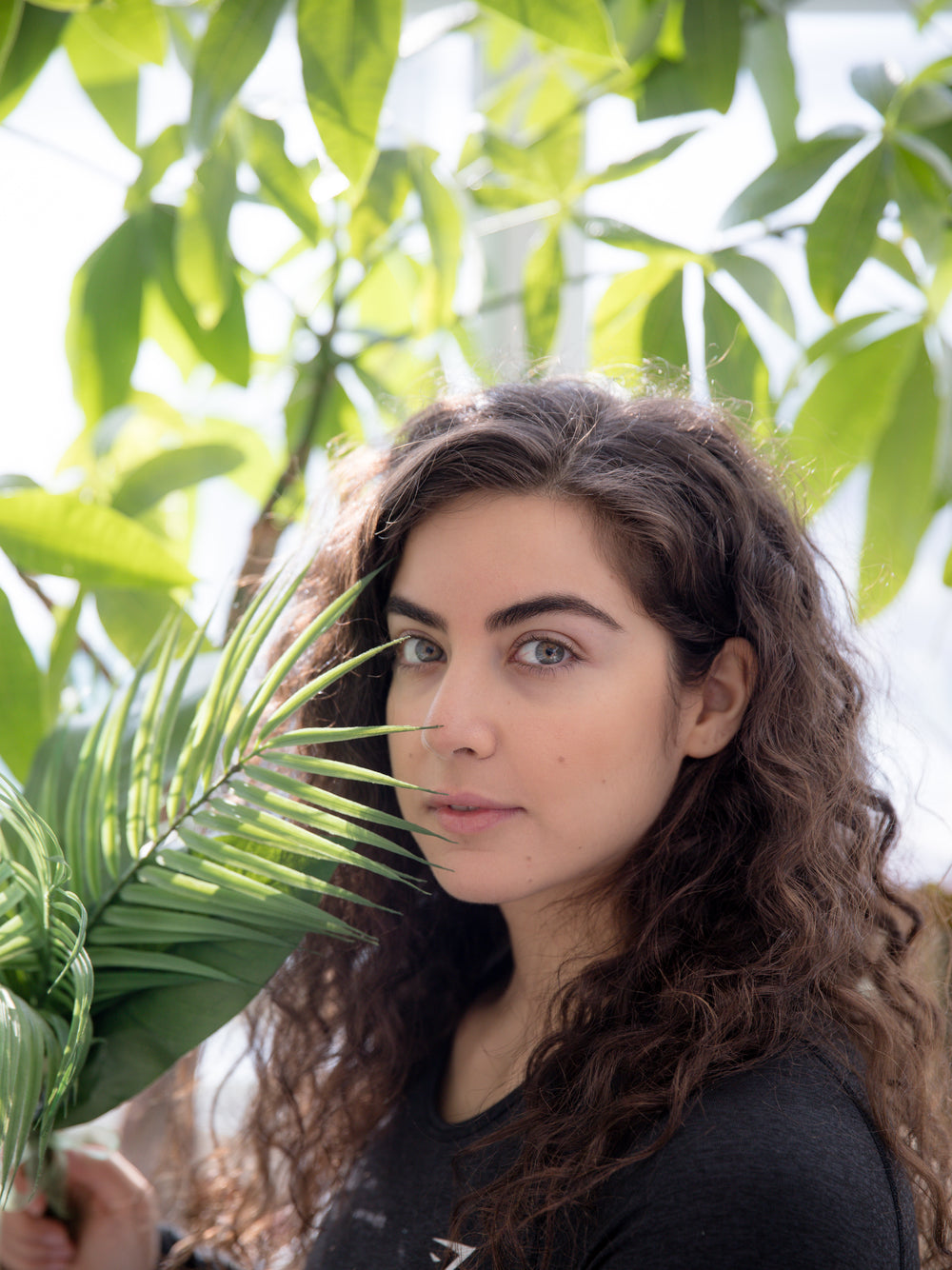 person with long curly hair surrounded by green leaves