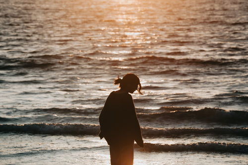 person with long hair silhouetted at sunset by the water