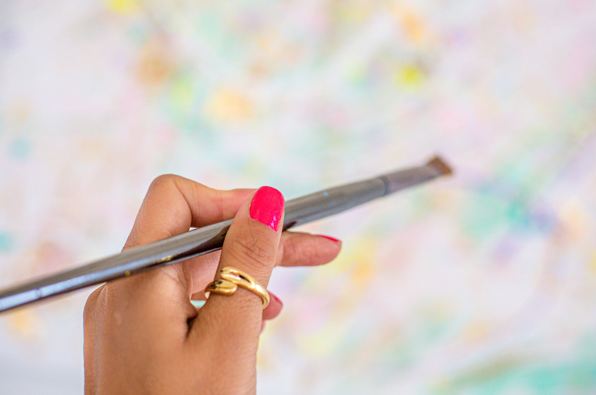 person with pink nail polish holds a silver paint brush