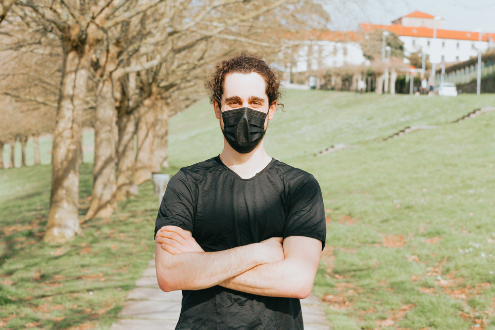 person with their arms crossed and wearing a facemask