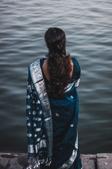 person wrapped in blue and silver looks out to water