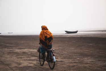 person wrapped in orange rides their bike on the beach