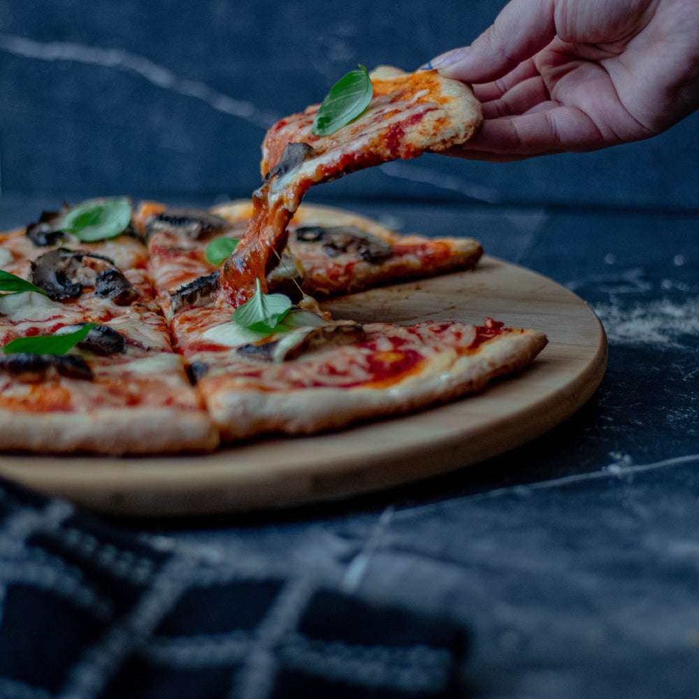 persons hand lifts a slice of pizza from round plate