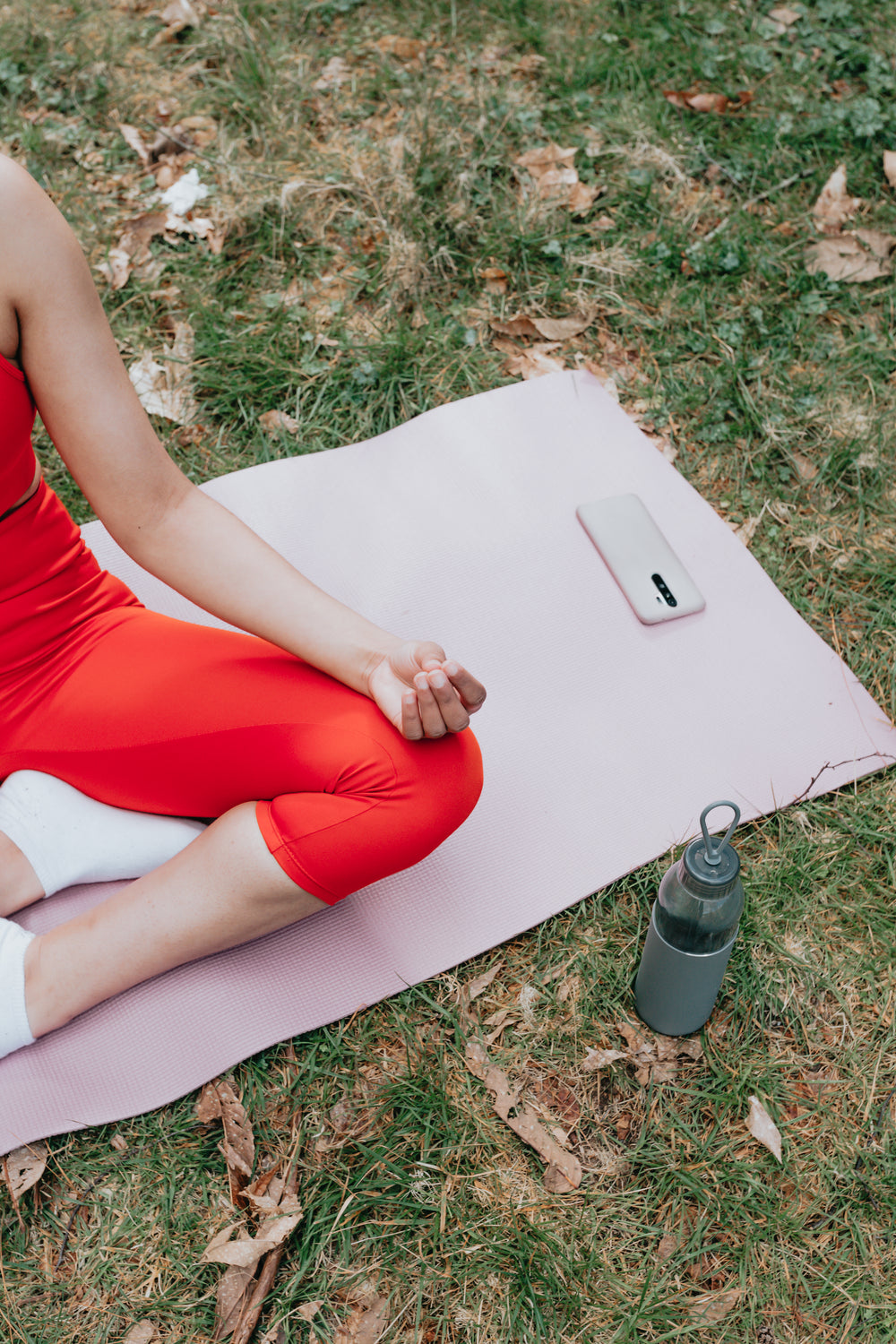 persons legs sitting on a pink yoga mat outdoors