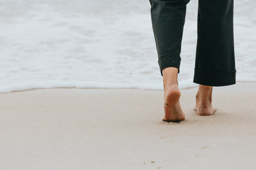 persons legs walking towards the water on a beach