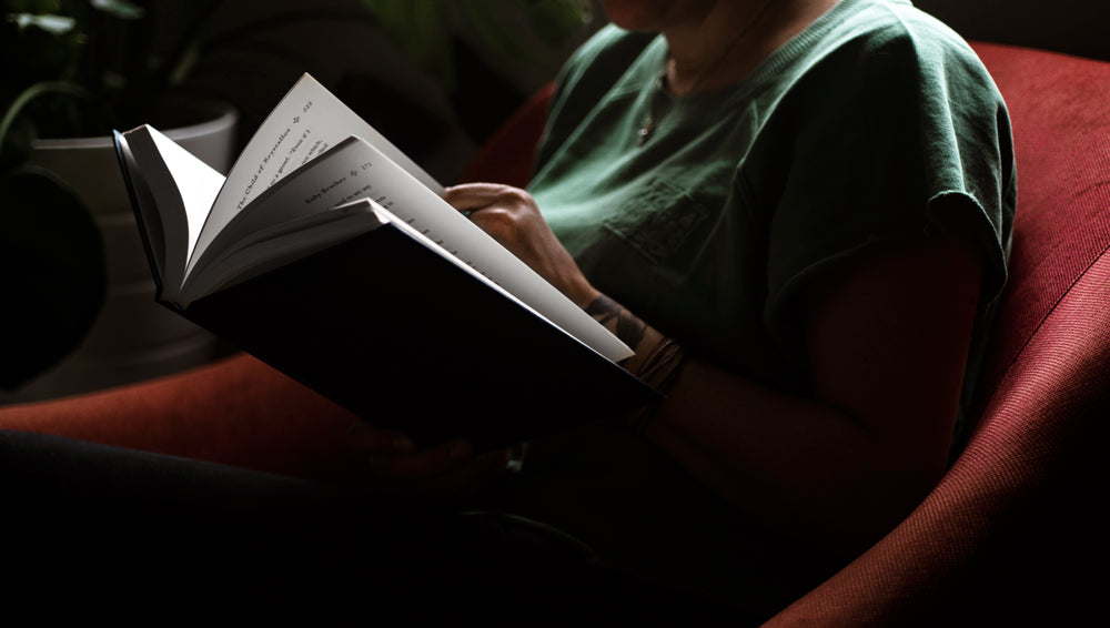 persons torso in a green shirt reads a hardcover novel