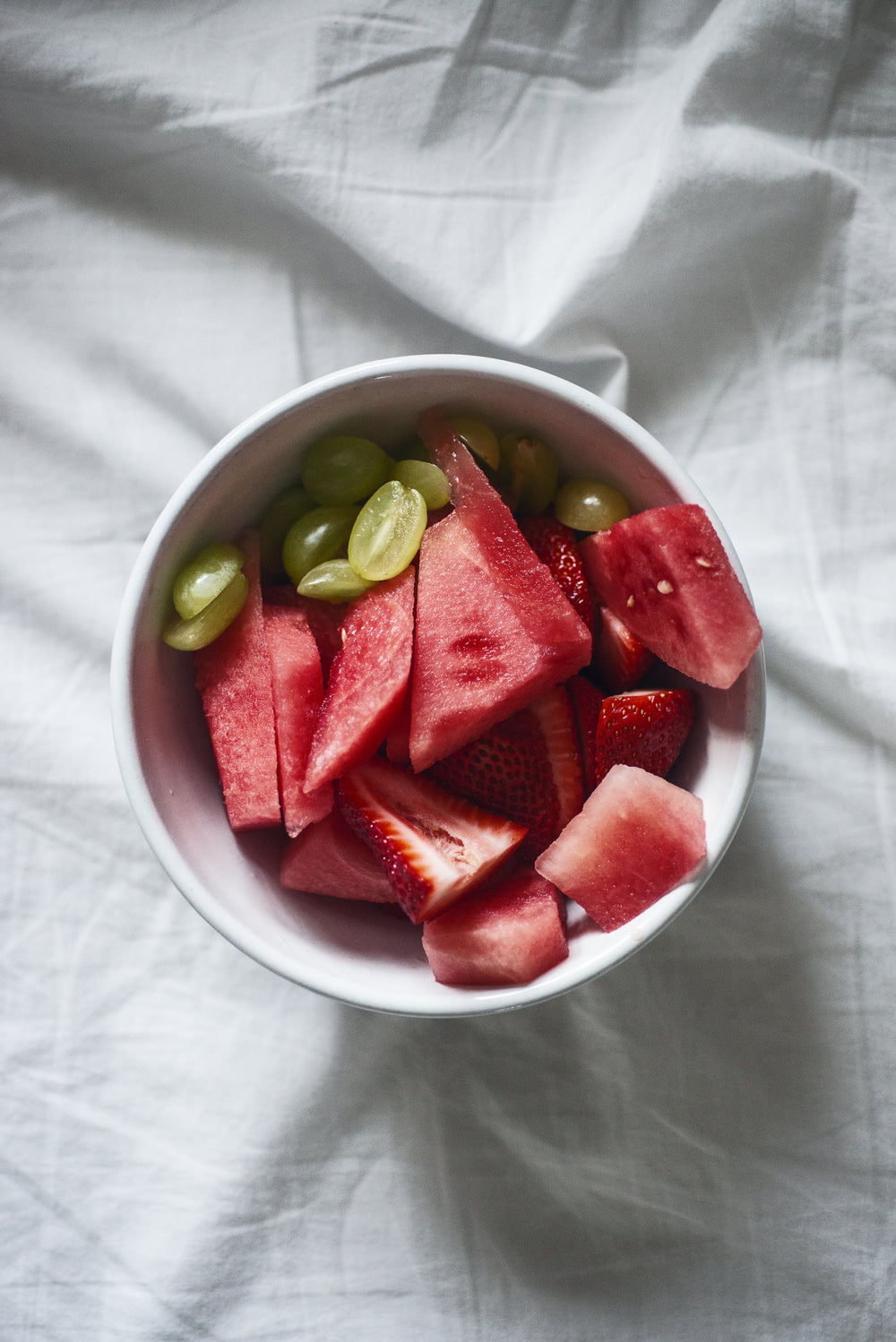 photo of a bowl of sliced fruit on a white sheet