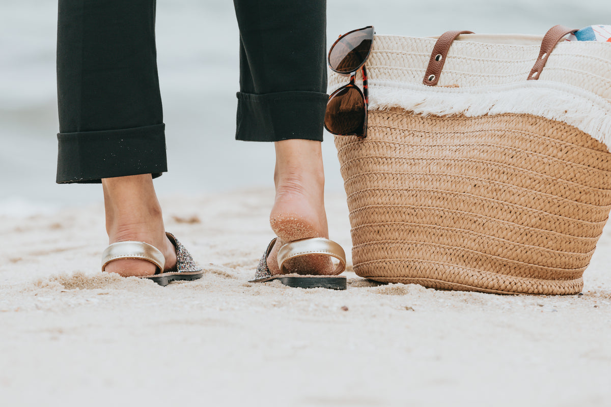 photo of a legs standing on a sandy beach next to a beach bag