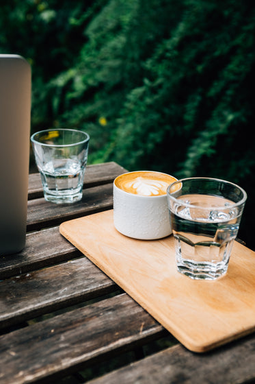 picnic table with a wooden tray holding a latte and a water