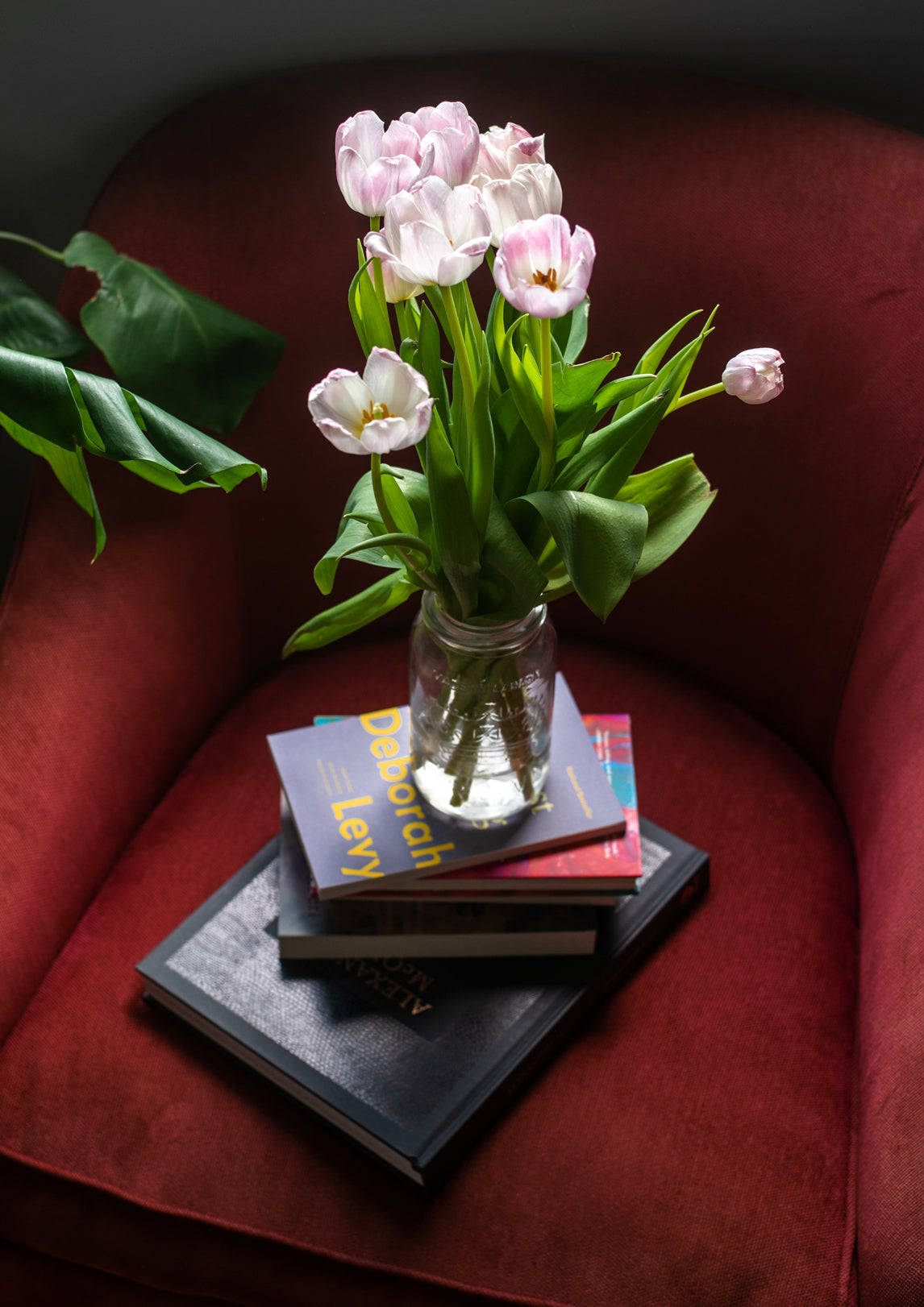 pink tulips on a glass jar on top of a stack of books