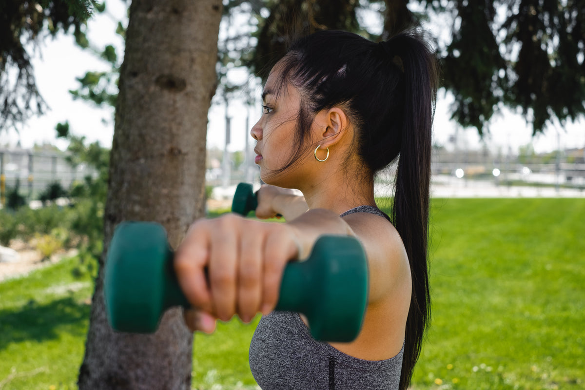 profile of a woman who is holding hand weights outdoors