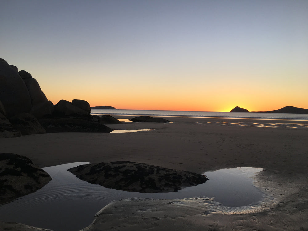 puddles of water on the beach reflect the sunset
