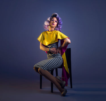 purple haired drag queen poses in chair