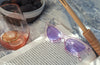 purple retro sunglasses lay on a open novel in the sunshine