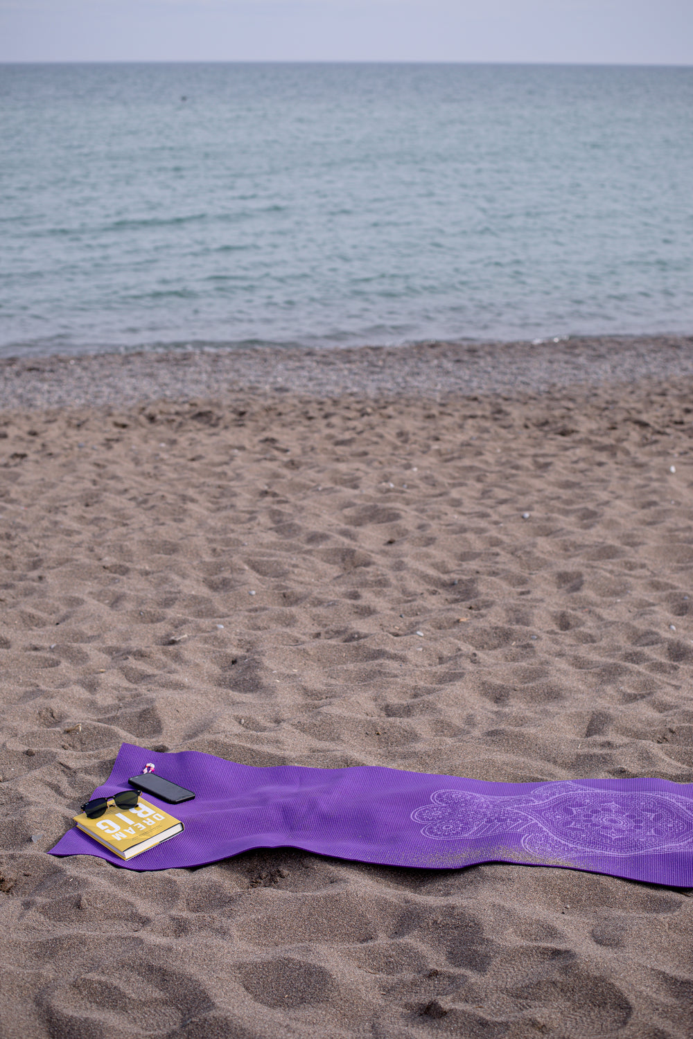 purple towel on a beach with book and cellphone