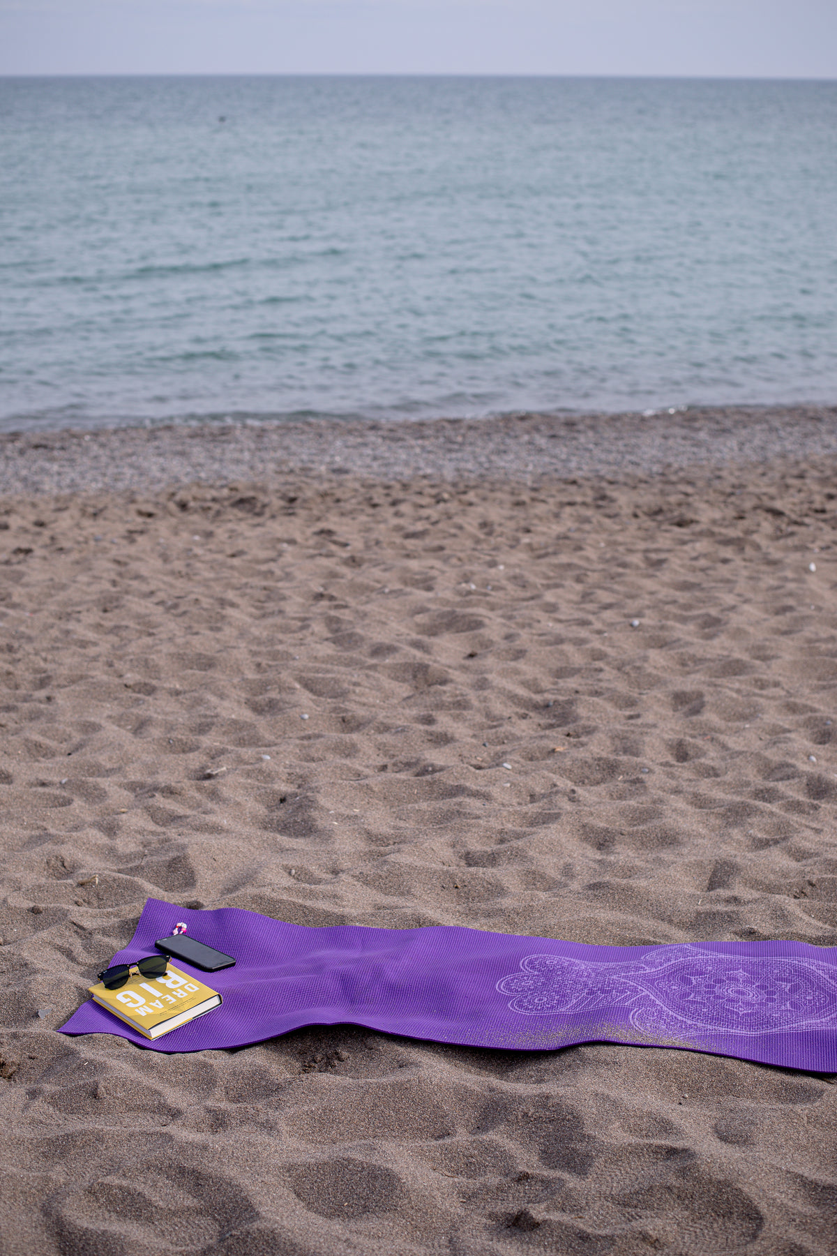 purple towel on a beach with book and cellphone