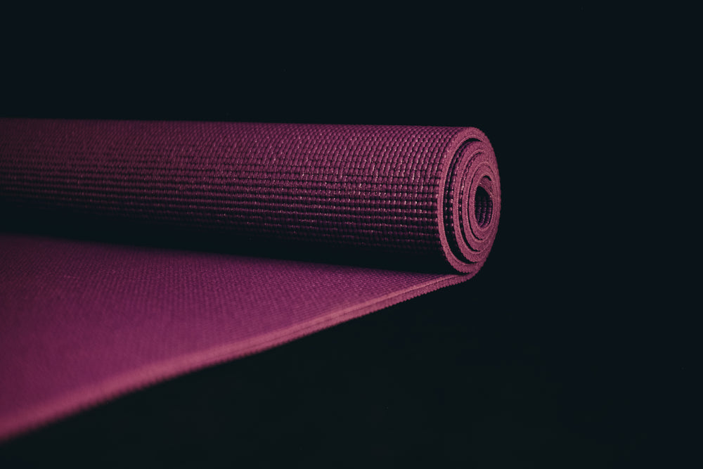 purple yoga mat partially rolled up on black