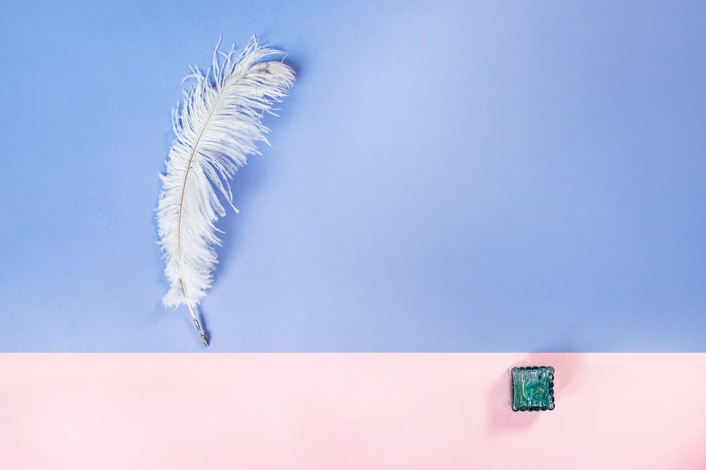 quill and ink bottle on blue and pink background