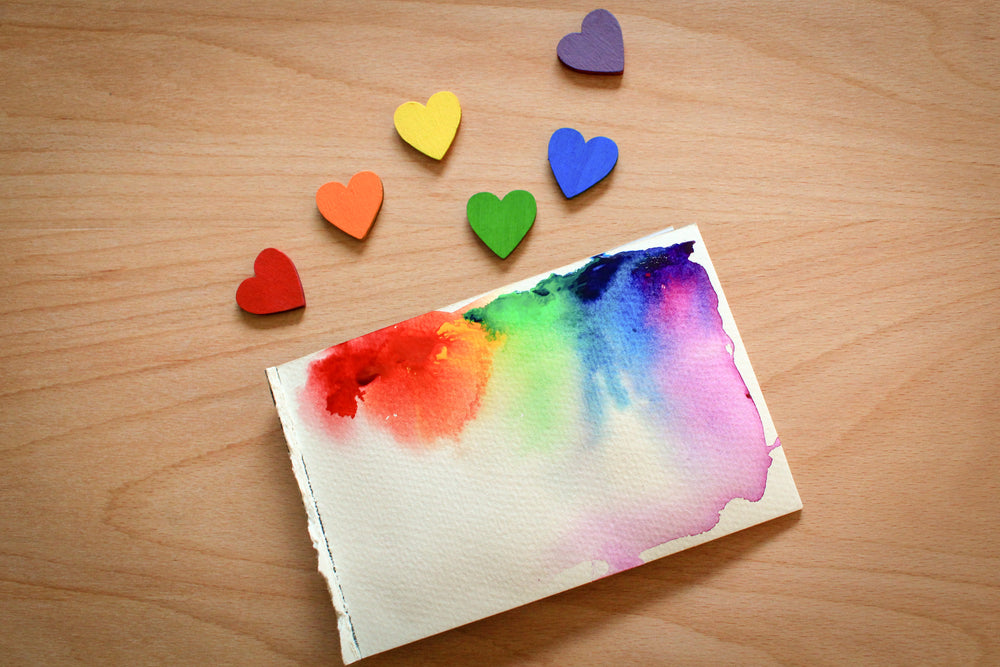 rainbow painted wooden hearts beside watercolour canvas