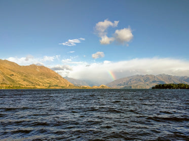 rainbow reaches for clouds over hills