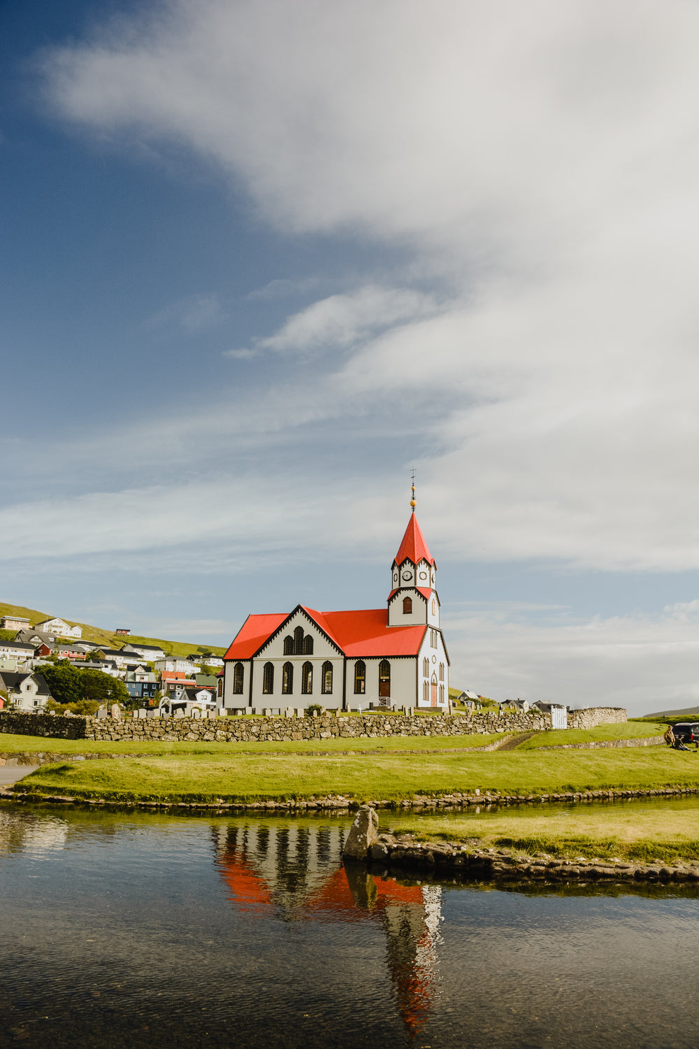 red and white church of sandavagur reflecting on waterfront