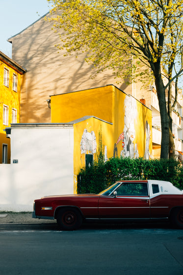 red classic car in front of yellow building