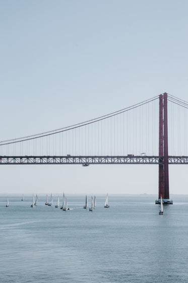 red suspension bridge over waterway filled with sailboats