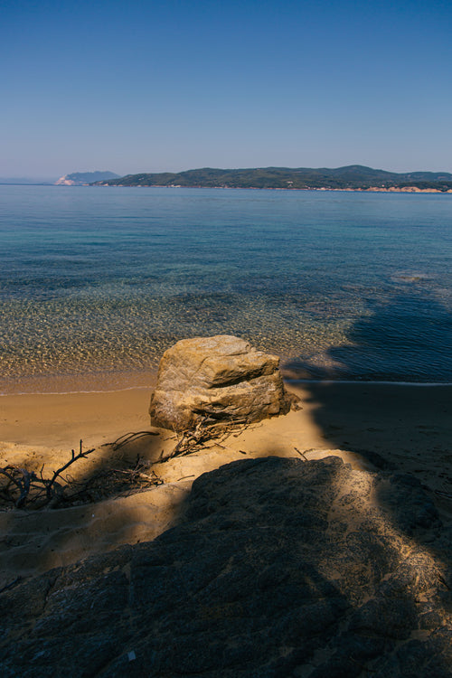 rock sits upon sandy sea shore