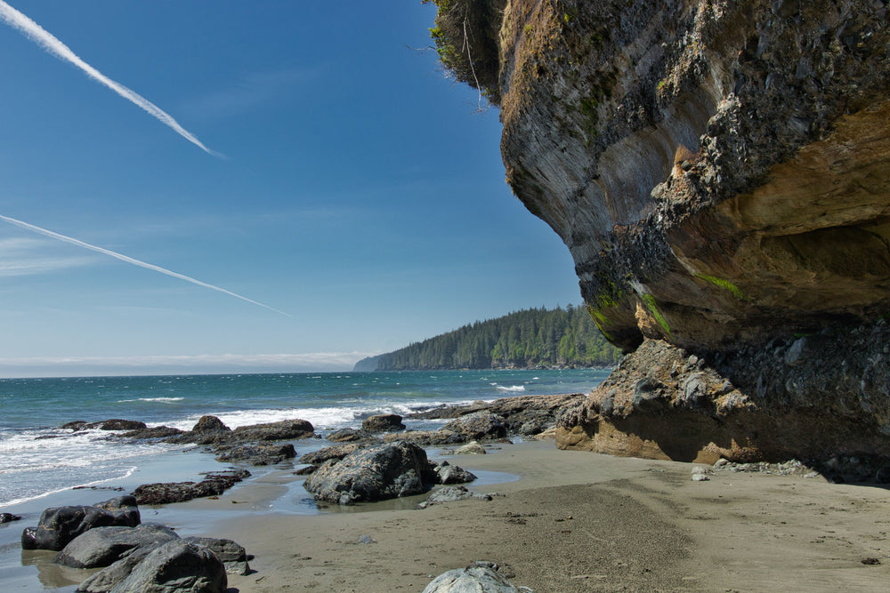 rocky cliff hangs over a sandy beach next to blue water