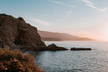 rocky cliffs crumble into pacific ocean under summer sunset