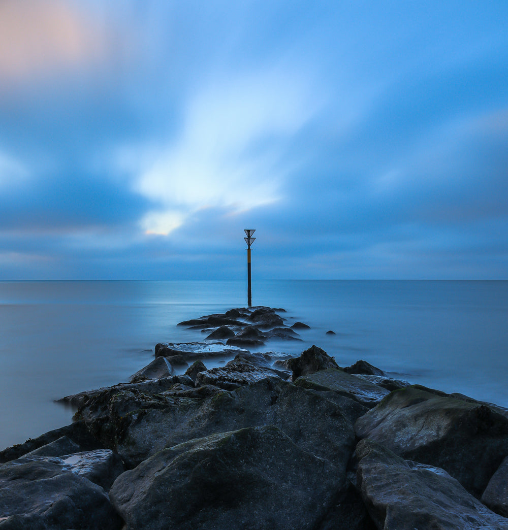 Rocky Shore Line Reaches Out To Still Blue Water