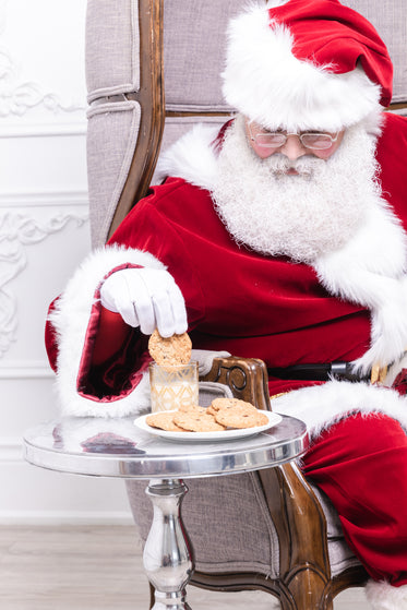 santa dips a cookie in a glass of milk