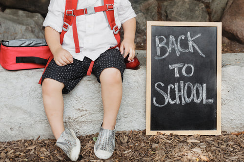 school kid sits by back to school sign