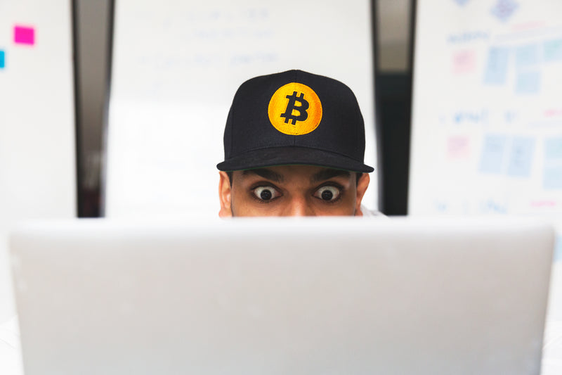 shocked bitcoin investor on laptop - a man wearing a hat