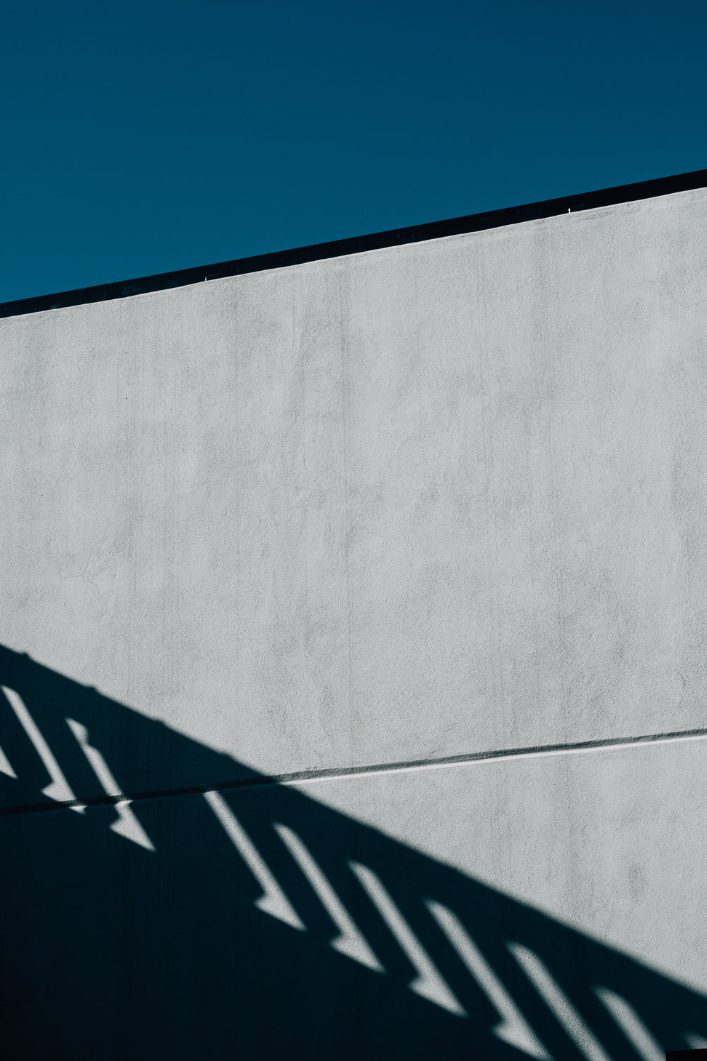 side of a building with no windows and a fences shadow