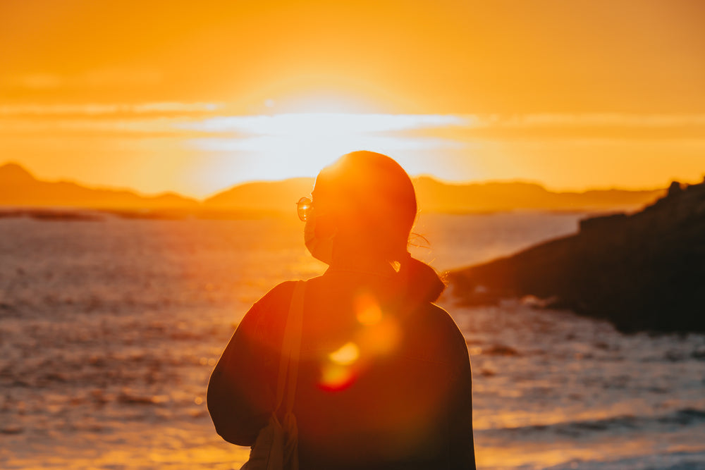 silhouette of a person looking out at the water at sunset