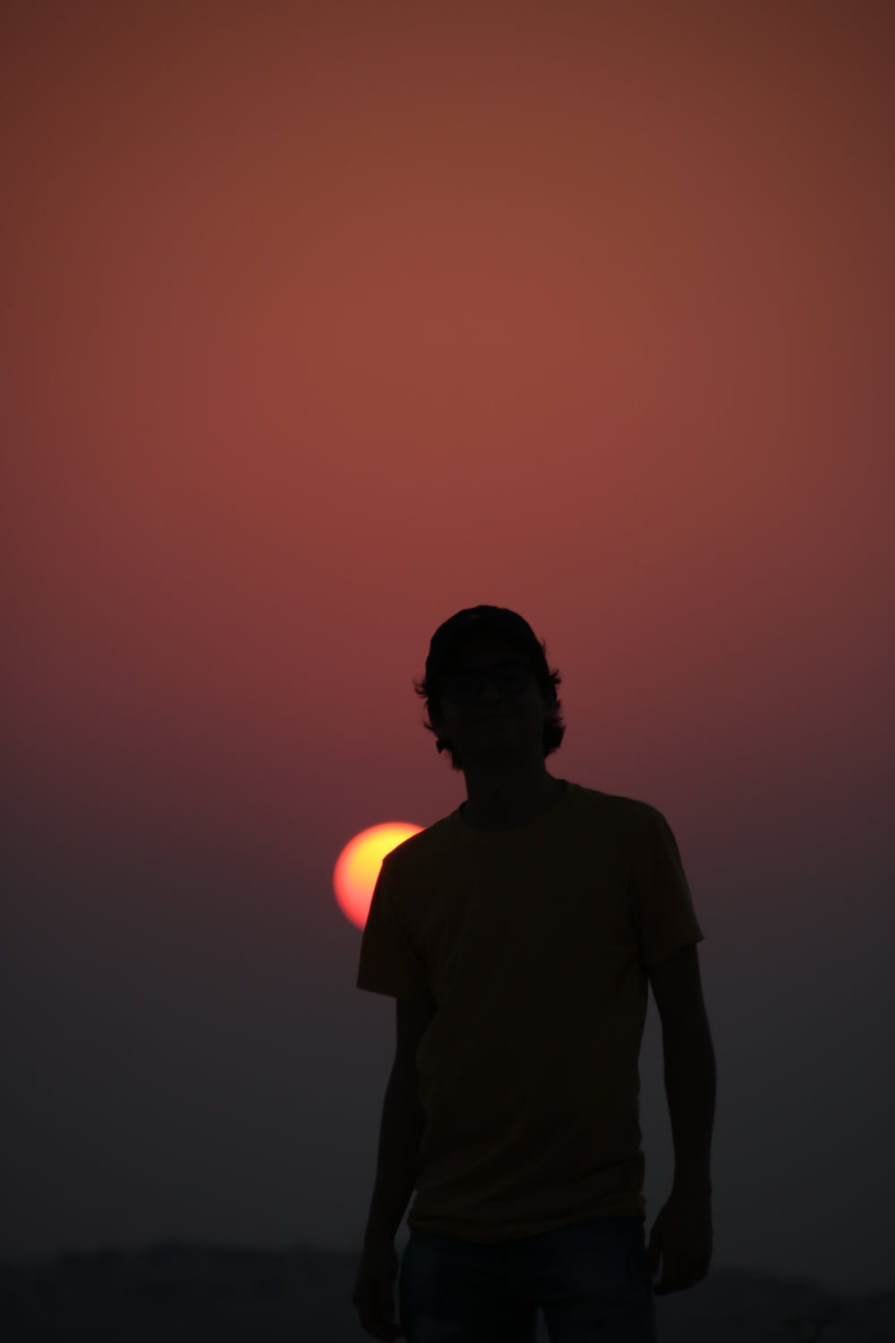 silhouette of a person with a baseball cap against a setting sun
