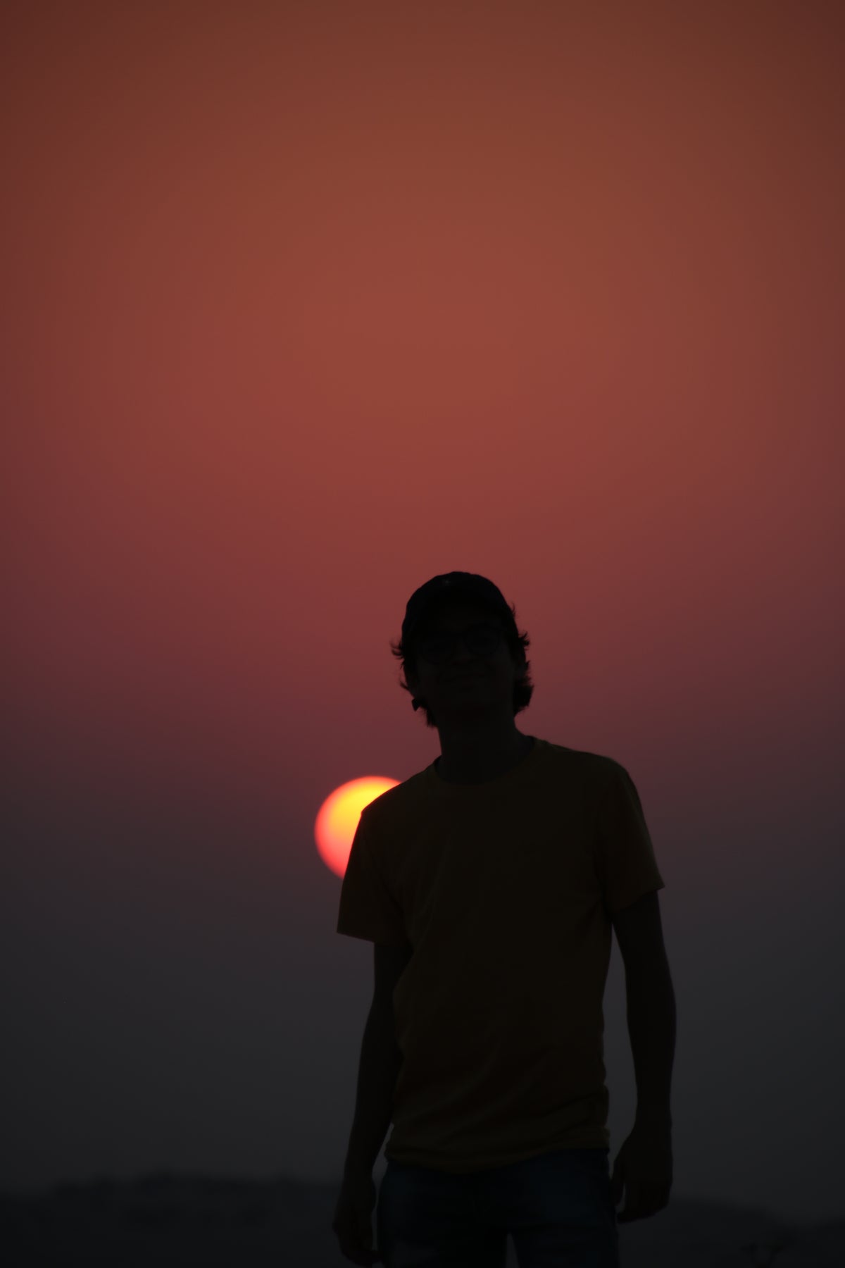 silhouette of a person with a baseball cap against a setting sun