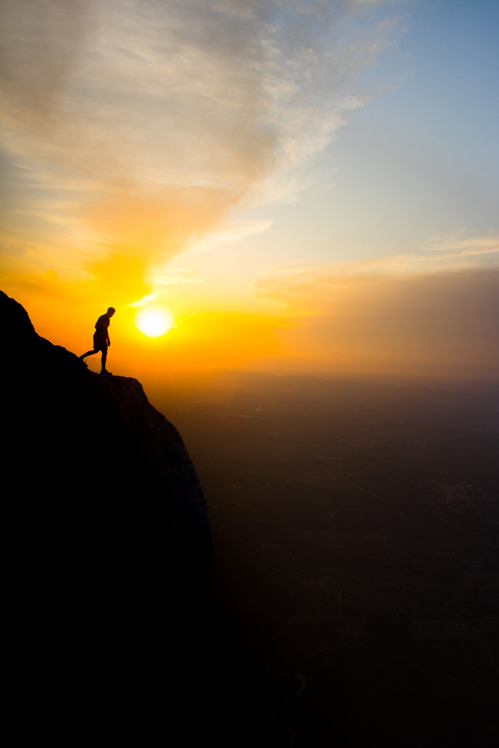 silhouette of person standing on a cliff at sunset
