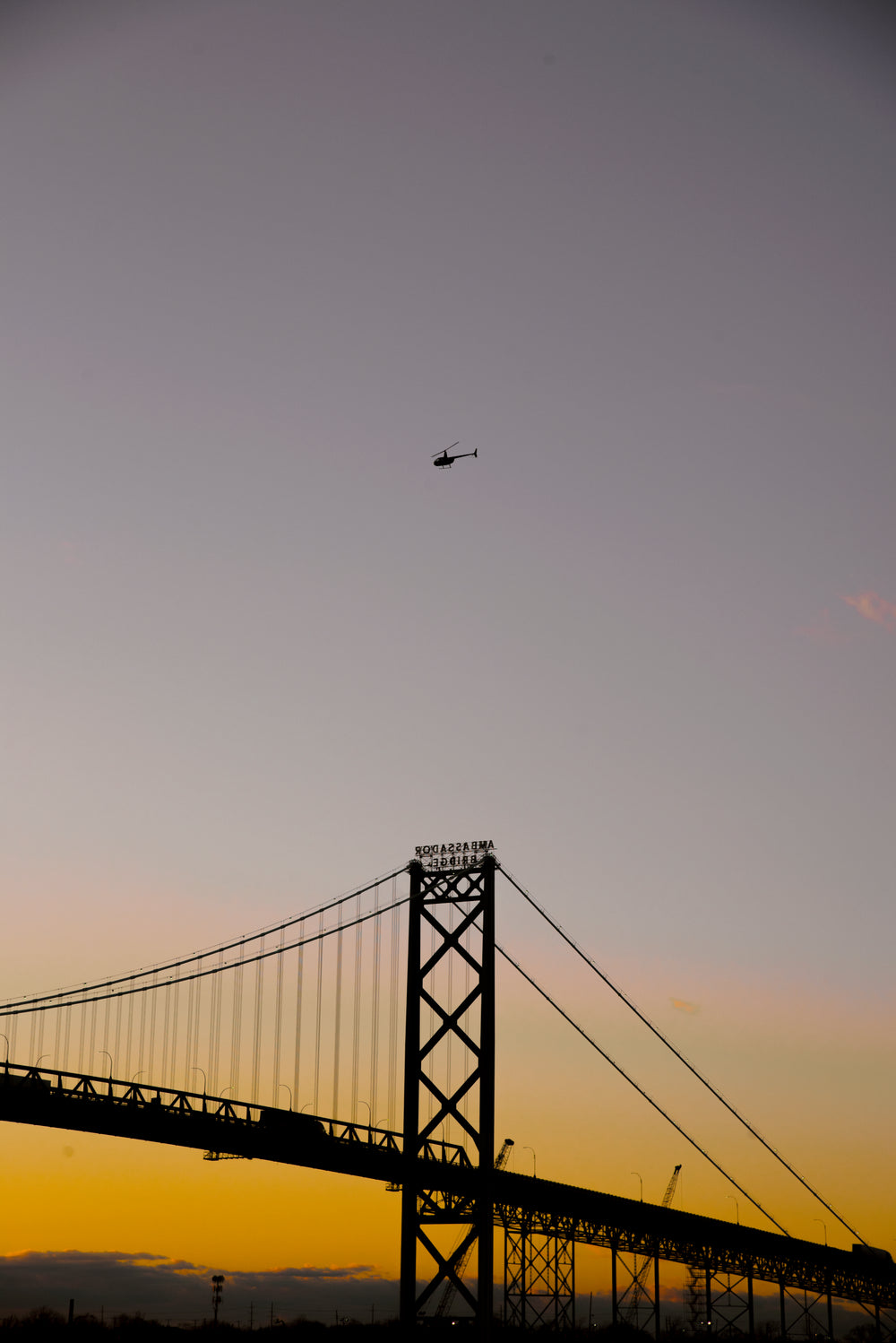 silhouetted large bridge and a helicopter at sunset